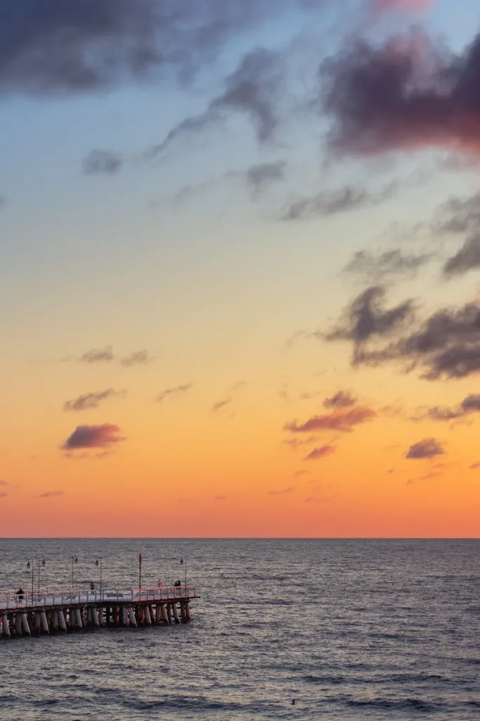Beautiful sunset over a calm ocean with a wooden pier extending into the water, creating a serene seascape.